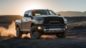 A stunning image of the Dodge Ram 2018, showcasing its powerful presence from the best possible angle. The truck is positioned on a rugged terrain, with its tires kicking up dirt and dust. The sun is setting behind the truck, casting a warm golden hue on the vehicle. The background features a vast open landscape, with rolling hills, distant mountains, and a sense of adventure and exploration.