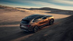 A stunning photograph of a sleek and modern SUV, captured from an elevated angle. The vehicle is positioned on a gentle slope in a vast, open desert landscape. The SUV's design is accentuated by the golden light reflecting off its surface, giving it a sense of luxury and sophistication. The background features a panoramic view of sand dunes, a serene blue sky, and the gentle sweep of the desert horizon.